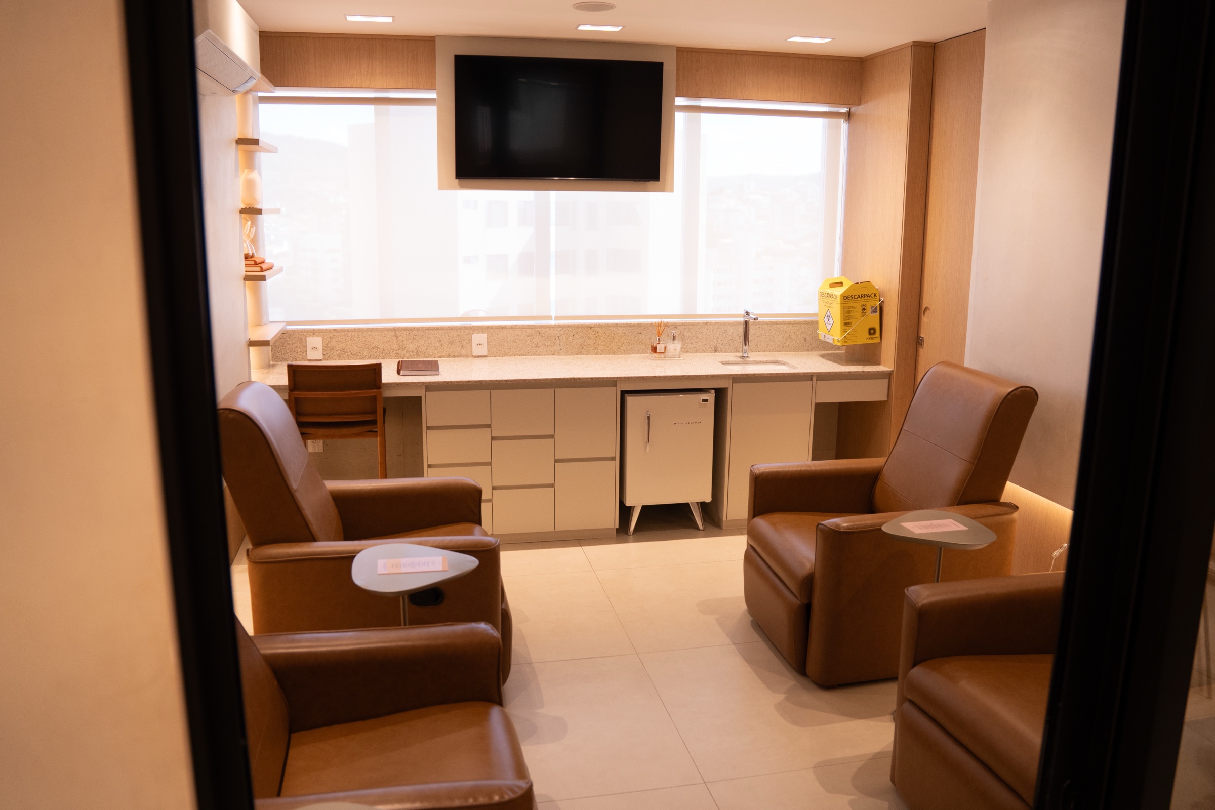 Sala de terapias injetáveis com poltronas de couro e vista da cidade